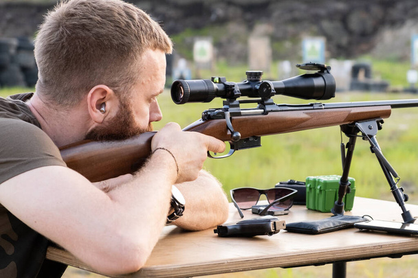 A man with glasses with a beard holds a sniper rifle - Photo, Image