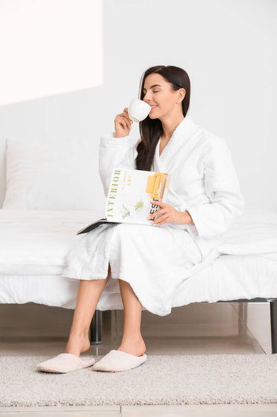 Ochtend van mooie jonge vrouw lezen tijdschrift en het drinken van koffie in de slaapkamer - Foto, afbeelding