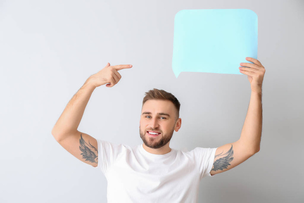 Young man with blank speech bubble on light background - Photo, Image