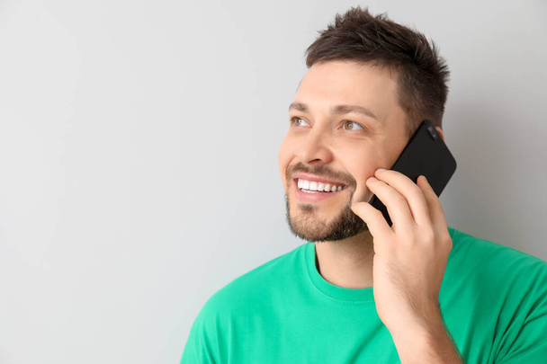 Happy man talking by mobile phone on light background - Foto, Imagen