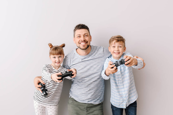 Vater und seine kleinen Kinder spielen Videospiele auf grauem Hintergrund - Foto, Bild