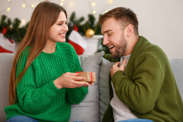 Щаслива жінка дарує подарунок своєму хлопцеві вдома напередодні Різдва
 - Фото, зображення