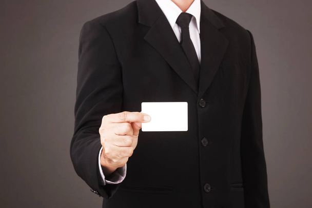 Férfi öltönyben tartó fehér névjegykártya elszigetelt szürke háttér - Fotó, kép