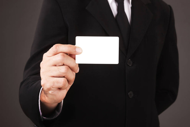 Άνδρας με κοστούμι που κρατά λευκή επαγγελματική κάρτα απομονωμένη σε γκρι φόντο - Φωτογραφία, εικόνα