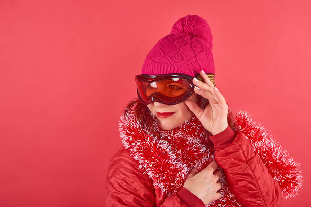 Studio shot πορτρέτο γυναίκα φορώντας rad ρούχα σκι και μάσκα στέκεται σε κόκκινο φόντο με tinsel - Φωτογραφία, εικόνα