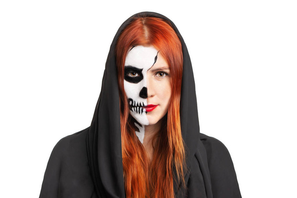 Retrato de una chica joven con maquillaje de cráneo de Halloween en una sudadera con capucha negra con pelo rojo
 - Foto, imagen