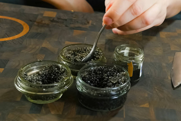 Stirring black caviar with a spoon in glass jar. - Photo, Image