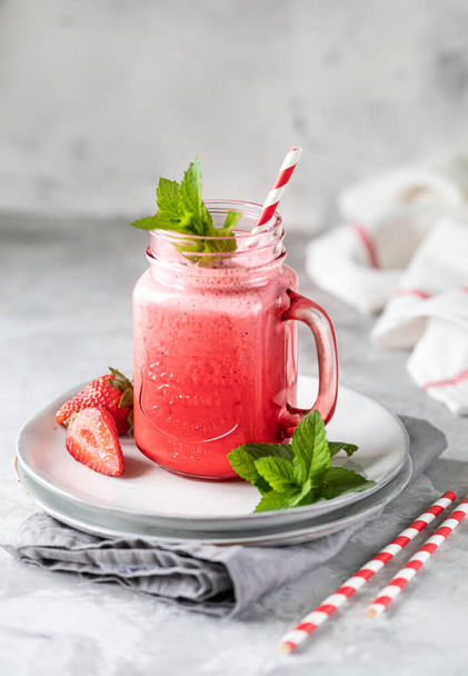 Eper és tej vagy joghurt smoothies egy gyönyörű piros üveg üveg és sprigs menta egy fehér beton asztalon. Az ünnepi Valentin-nap receptje. Fénymásolási hely - Fotó, kép