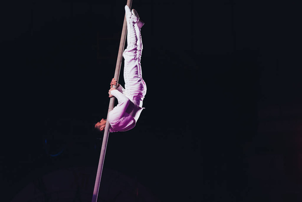 KYIV, UKRAINE - NOVEMBER 1, 2019: Side view of flexible air gymnast performing with pole in circus isolated on black - Foto, Bild