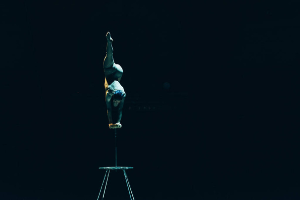 KYIV, UKRAINE - NOVEMBER 1, 2019: Back view of flexible acrobat balancing on hands in circus isolated on black - Foto, Imagem