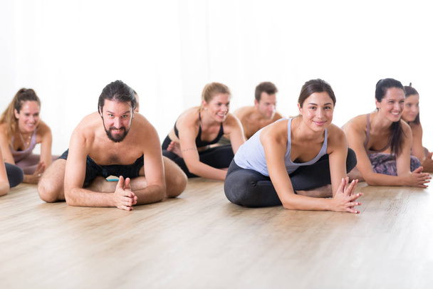 Grupa młodych, atrakcyjnych sportowców w studio jogi, ćwiczących lekcję jogi z instruktorem, siedzących na podłodze w przednim zespole rozciągającym pozycję do jogi. Zdrowy aktywny tryb życia, ćwiczenie na siłowni - Zdjęcie, obraz