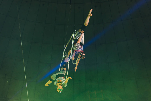 KYIV, UCRANIA - 1 DE NOVIEMBRE DE 2019: Vista de ángulo bajo de gimnastas de aire flexibles haciendo split mientras realizan con anillos en circo
 - Foto, imagen