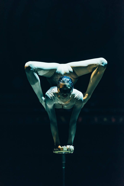 KYIV, UKRAINE - NOVEMBER 1, 2019: Flexible gymnast performing handstand in circus isolated on black - Фото, изображение