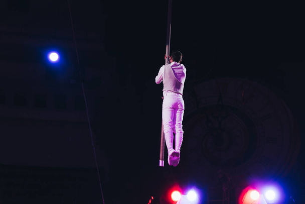 KYIV, UKRAINE - NOVEMBER 1, 2019: Back view of air gymnast with pole and light of floodlights in circus isolated on black - 写真・画像