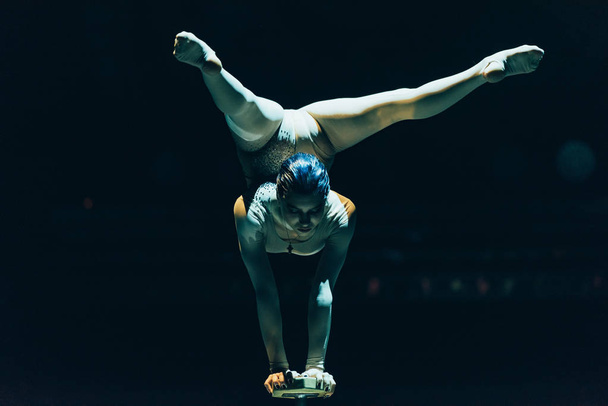 KYIV, UKRAINE - NOVEMBER 1, 2019: Gymnast doing handstand in circus isolated on black - Foto, imagen