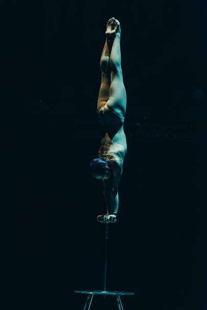 KYIV, UKRAINE - NOVEMBER 1, 2019: Gymnast performing handstand in circus isolated on black - Photo, Image