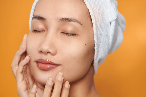 Face of Asian woman smiling and touching her face ,wear towel. Skincare and Cosmetology concept,on orange background - Foto, Bild