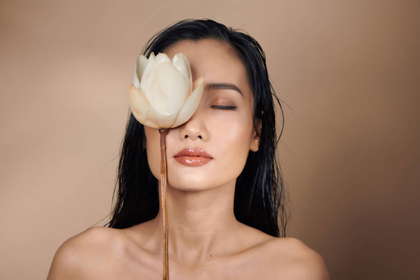 Hermosa chica asiática joven con maquillaje natural y el pelo mojado posando en el estudio sobre un fondo beige
  - Foto, imagen