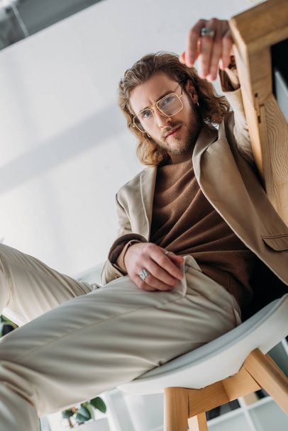 selective focus of elegant fashionable businessman posing on chair in office - Fotoğraf, Görsel
