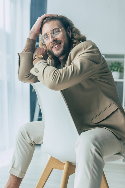 smiling elegant fashionable businessman posing on chair in office - Foto, Imagem