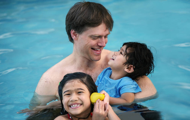 Pai caucasiano na piscina com crianças biraciais, segurando incapacitante
 - Foto, Imagem