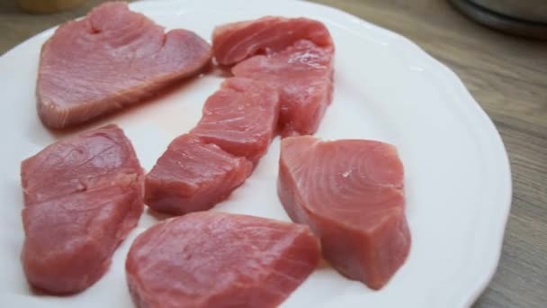 Juicy tuna fish steaks ready to cook. Lies on a white plate on the kitchen worktop. Male hand flips a piece of tuna. - Imágenes, Vídeo
