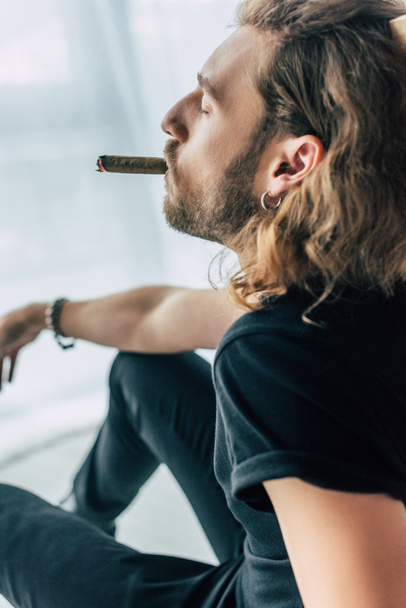 модний випадковий бізнесмен в загальному чорному вбранні куріння сигари з закритими очима в офісі
 - Фото, зображення