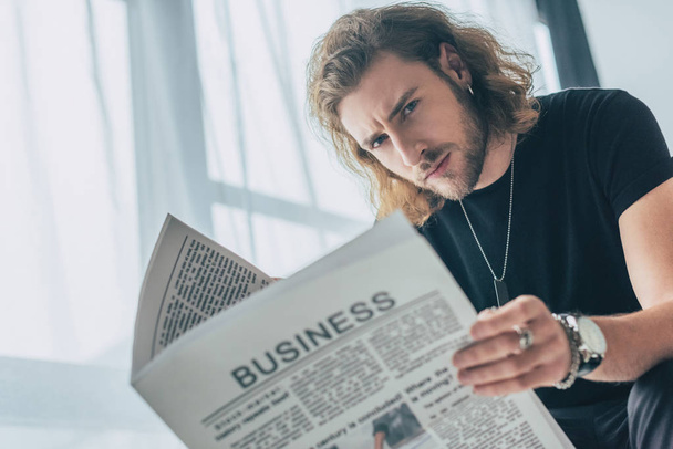selective focus of fashionable casual businessman in total black outfit holding business newspaper in office - Fotoğraf, Görsel