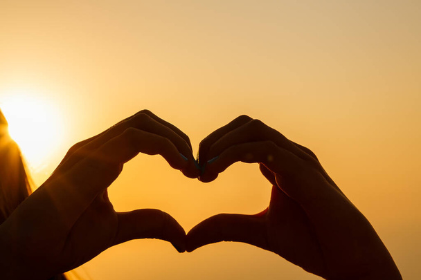 Жіночі руки роблять серце на розмитому фоні заходу сонця
 - Фото, зображення