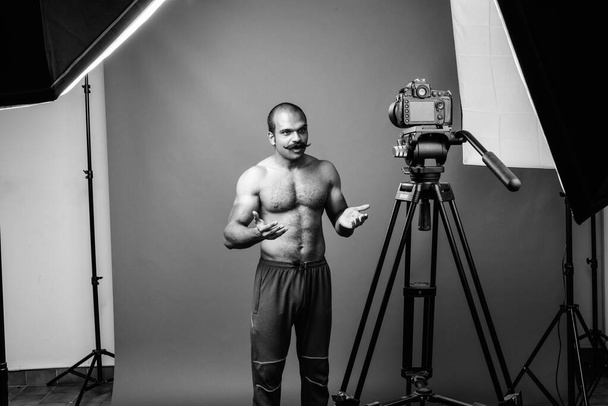 hombre indio musculoso sin camisa con bigote vlogging sobre fondo gris
 - Foto, Imagen