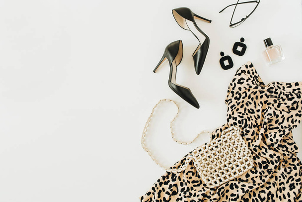 Moderne collage met vrouwelijke kleding en accessoires. Luipaard print jurk, hoge hak schoenen, oorbellen, glazen, portemonnee, parfum op witte achtergrond. Vlakke lay, bovenaanzicht. - Foto, afbeelding