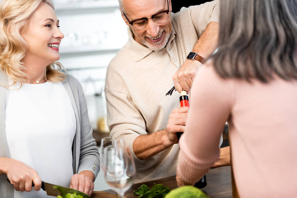 selective focus of man opening bottle with wine and woman cutting lettuce  - Photo, Image
