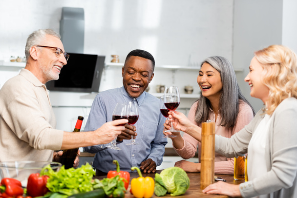 uśmiechnięci wielokulturowi przyjaciele brzęczący kieliszkami do wina w kuchni  - Zdjęcie, obraz