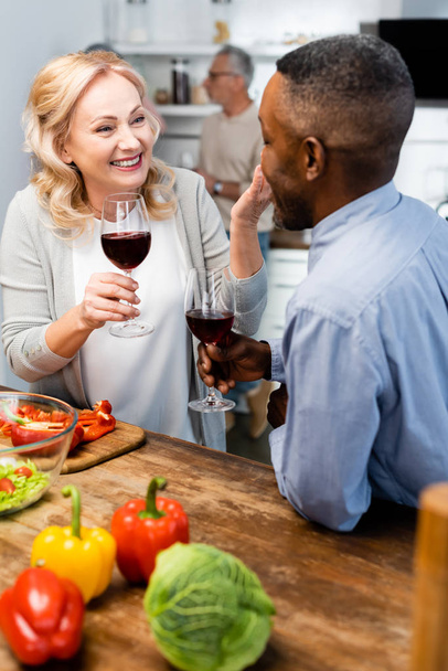 glimlachende vrouw en afrikaanse Amerikaanse man praten en het houden van wijnglazen - Foto, afbeelding