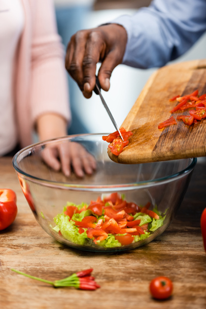 cropped view of african american man adding cut bell pepper to bowl and woman standing near him  - Photo, Image