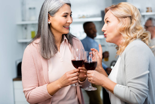 smiling woman talking with asian friend and holding wine glass  - Foto, immagini