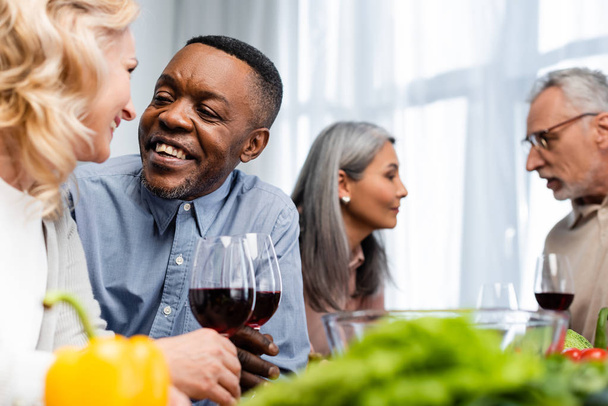 selective focus of multicultural friends talking and holding wine glasses  - Foto, afbeelding