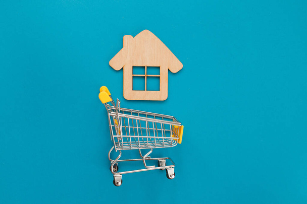 Kis bevásárlókosár játék fa ház kék színű papír lapos feküdt háttér. Jelzálog ingatlan biztosítás vásárolni álom home shopping sale rent concept - Fotó, kép