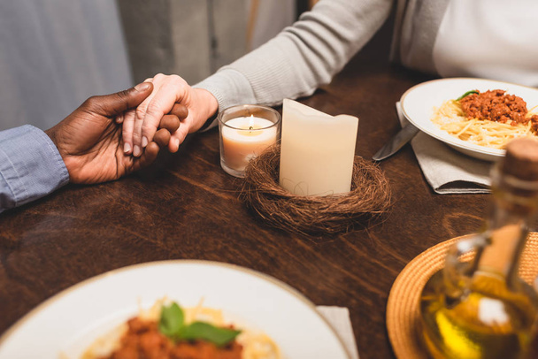 cropped view of african american man holding hand of friend and praying during dinner  - Φωτογραφία, εικόνα