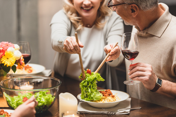 cropped view of smiling woman putting salad on plate of friend during dinner  - Photo, Image