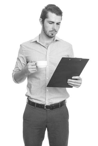 Young handsome Caucasian businessman reading clipboard while holding coffee cup - Photo, image