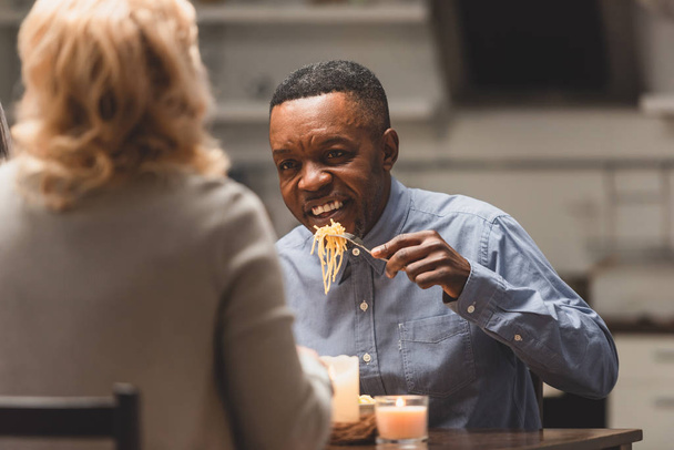 selective focus of smiling african american man eating pasta and talking with friend during dinner  - Foto, imagen