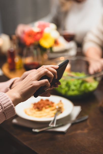 vista recortada de la mujer sosteniendo teléfono inteligente durante la cena
  - Foto, Imagen