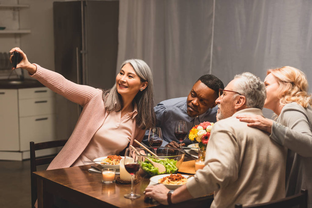 mosolygós multikulturális barátok csinál szelfi okostelefon vacsora közben  - Fotó, kép
