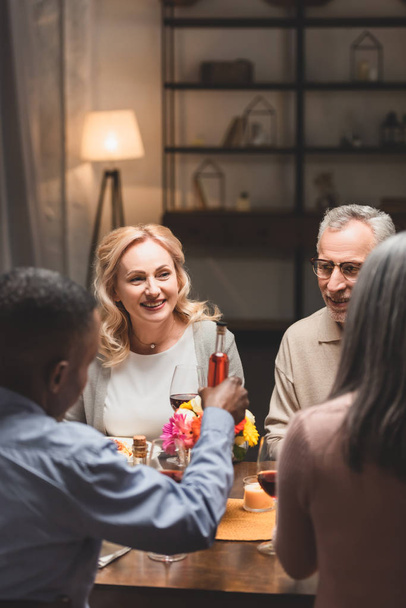 вибірковий фокус усміхненого чоловіка і жінки, що розмовляє з мультикультурними друзями під час вечері
  - Фото, зображення