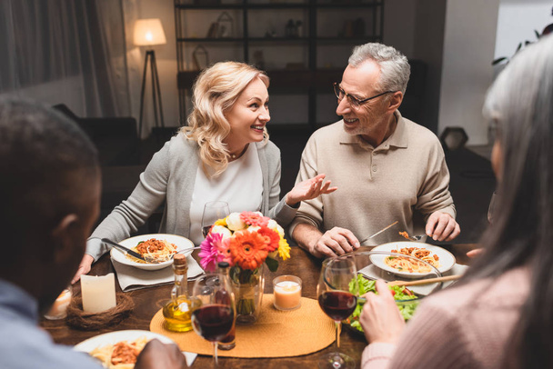 селективное внимание улыбающихся мужчин и женщин, беседующих с мультикультурными друзьями во время ужина
  - Фото, изображение