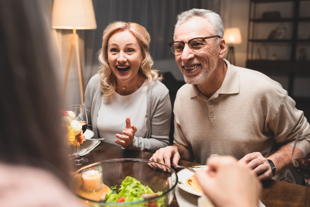enfoque selectivo de sonreír hombre y mujer hablando con un amigo durante la cena
  - Foto, Imagen