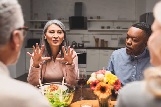 selectieve focus van multiculturele man en vrouw in gesprek met vrienden tijdens het diner  - Foto, afbeelding