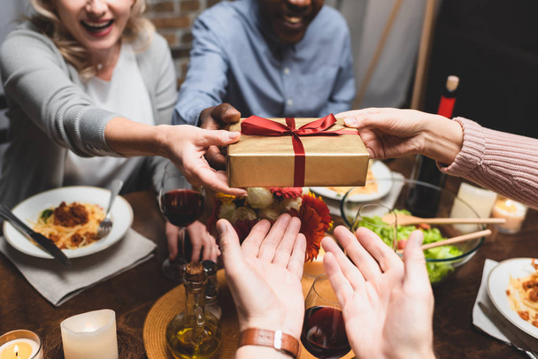 przycięty widok wielokulturowego mężczyzny i kobiety dając prezent dla przyjaciół podczas kolacji  - Zdjęcie, obraz