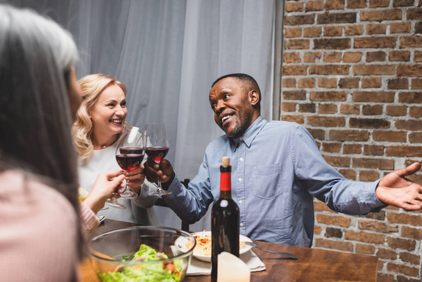 cropped view of woman clinking with smiling multicultural friends during dinner  - Foto, Bild
